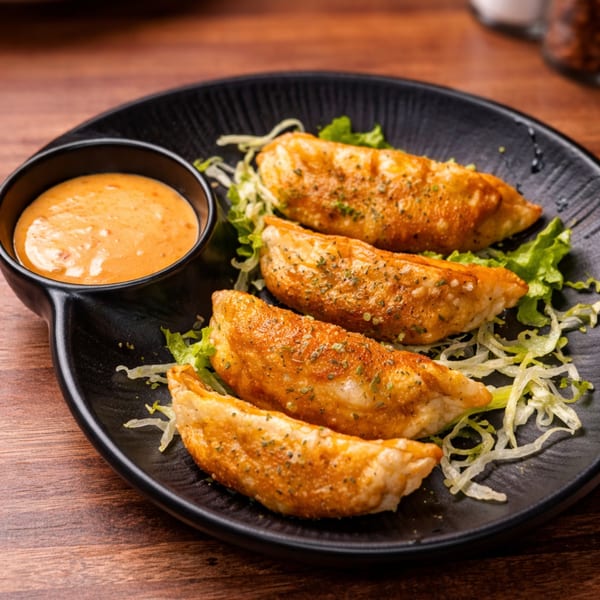 Four golden-brown fried dumplings with herbs on a bed of shredded lettuce, served with a side of orange dipping sauce.