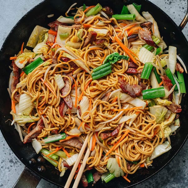 Close-up of a large wok filled with stir-fried noodles, vegetables, and meat, with chopsticks.